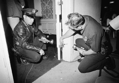 Two police officers identifying bullets in the door frame, shortly after the killing: